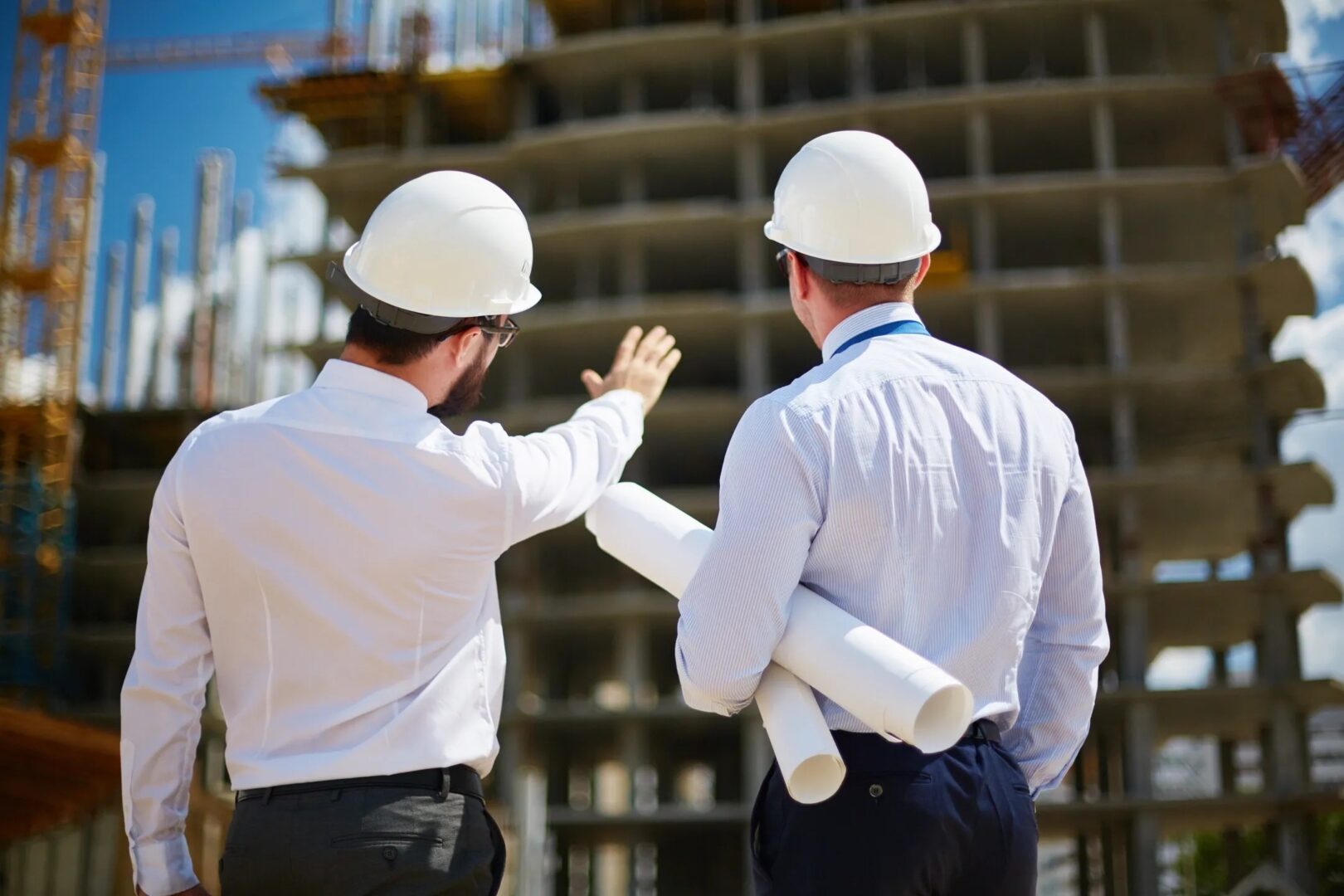Two men in white hard hats looking at a building.