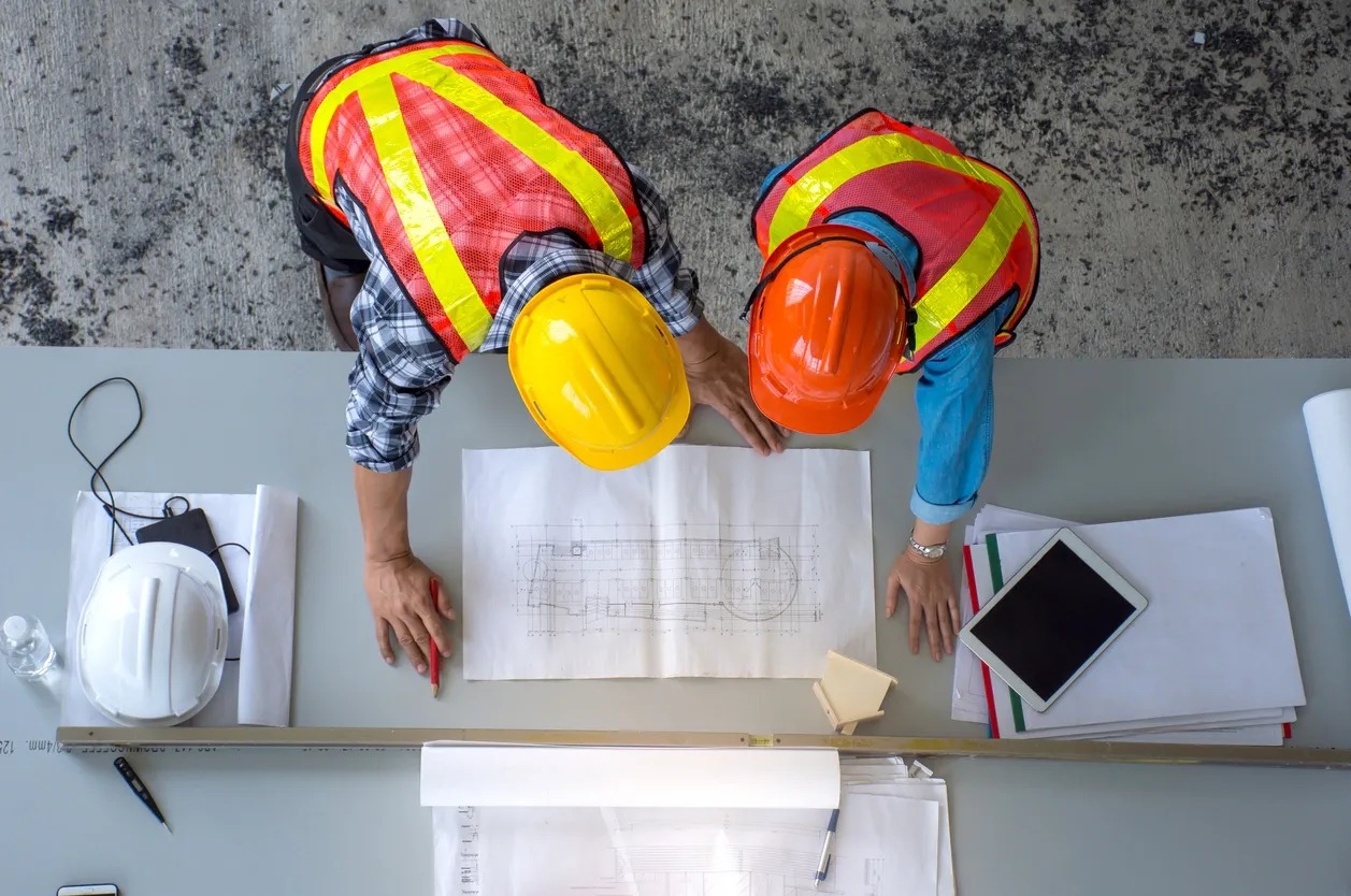 Two construction workers looking at a plan on top of the table.