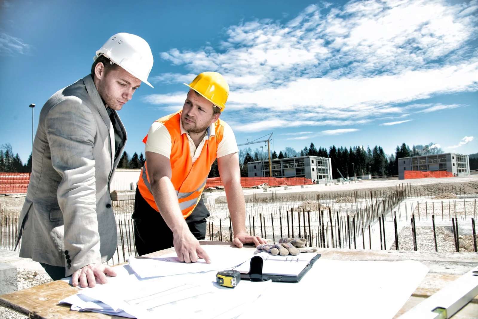 Two men in hard hats and vests looking at plans.