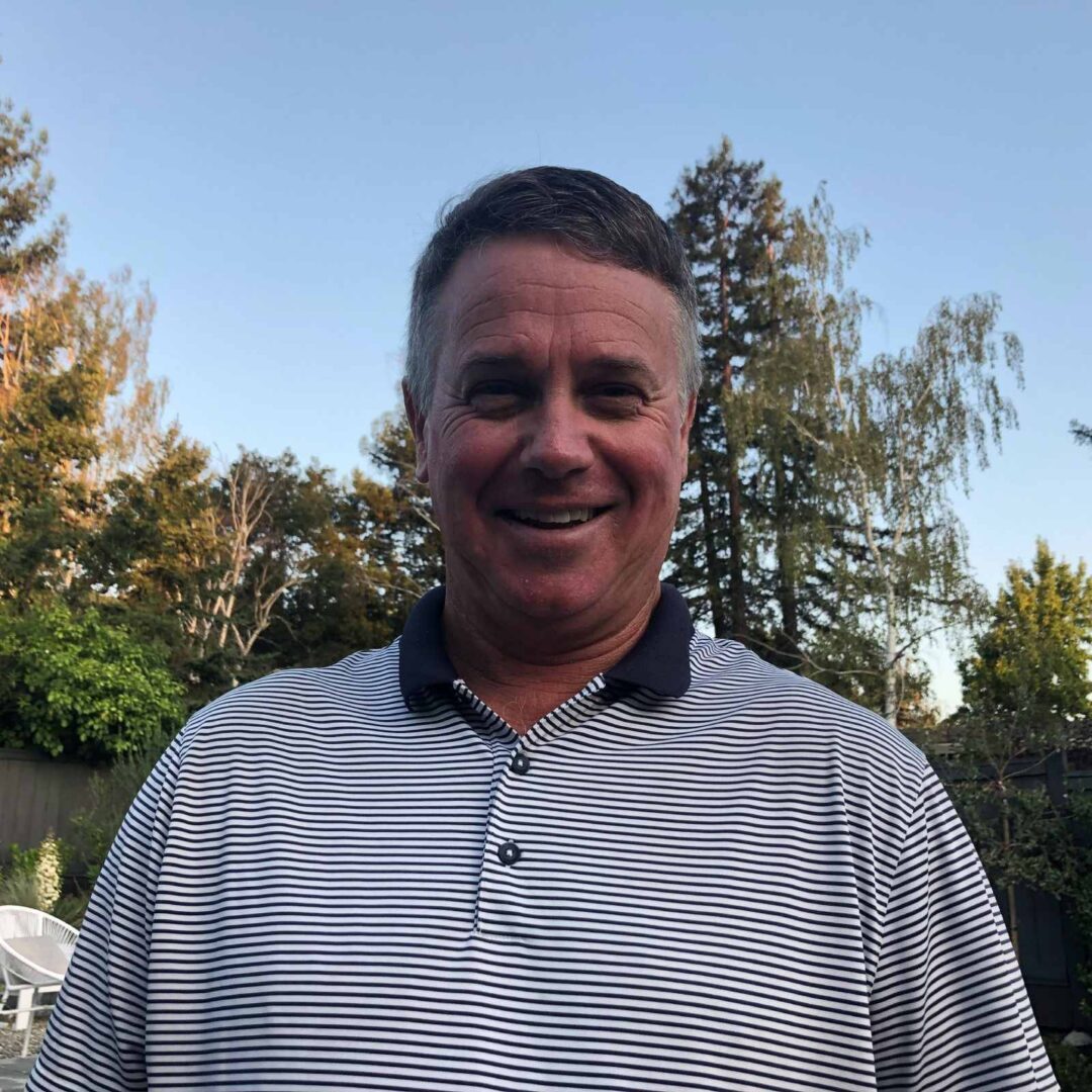 A man in striped shirt standing outside near trees.