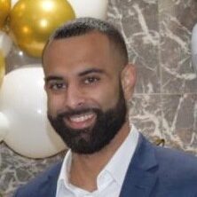 A man with beard and suit jacket standing in front of balloons.