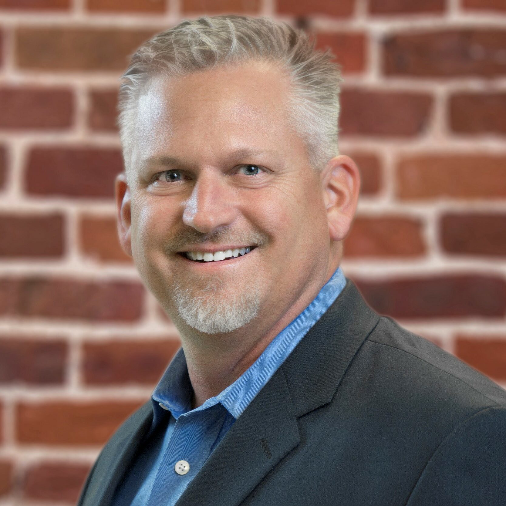 A man with grey hair and a blue shirt is smiling.